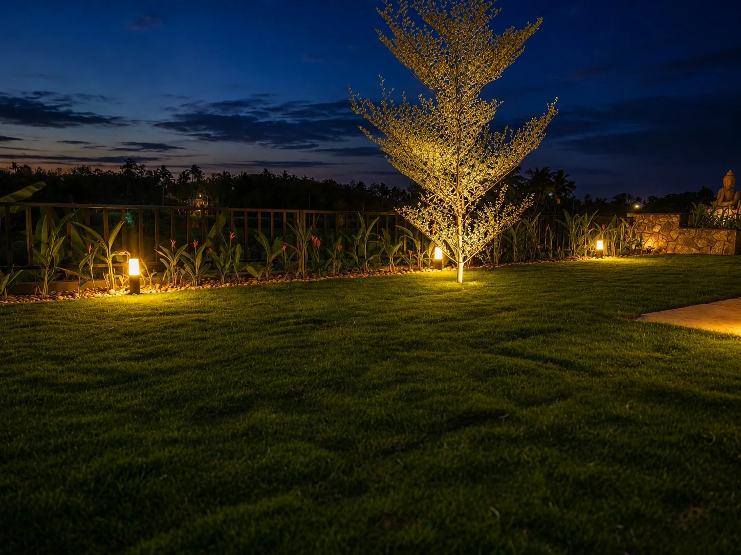 Tree uplighting and bollard path lights across a lawn at dusk